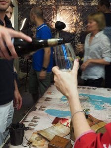 plusieurs joueurs autour du plateau de jeu escap'oenologik un homme sert un verre de vin