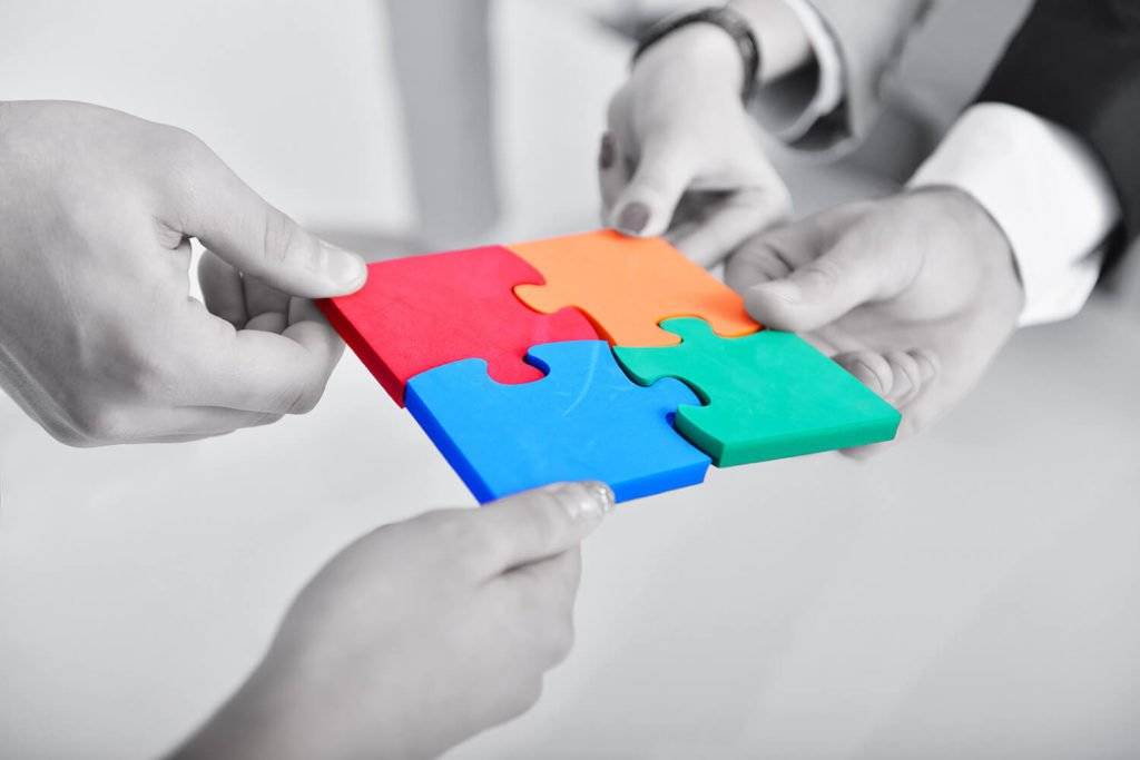 4 mains tiennent une pièce de puzzle de couleur à emboiter