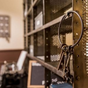 un gros trousseau de clés anciennes accrochées à un casier de prison en fer, en arrière plan une machine à écrire