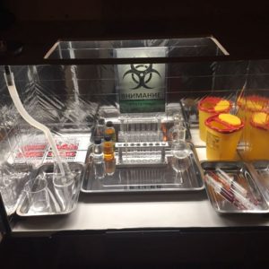 boîte de manipulation de produits chimiques dangereux, une pancarte écrite en russe, une boîte de déchets infectieux, des seringues remplies de sang, un becher, un porte tube à essais